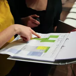 die Hände von zwei Menschen zeigen auf ein Blatt Papier mit einer Planungstabelle